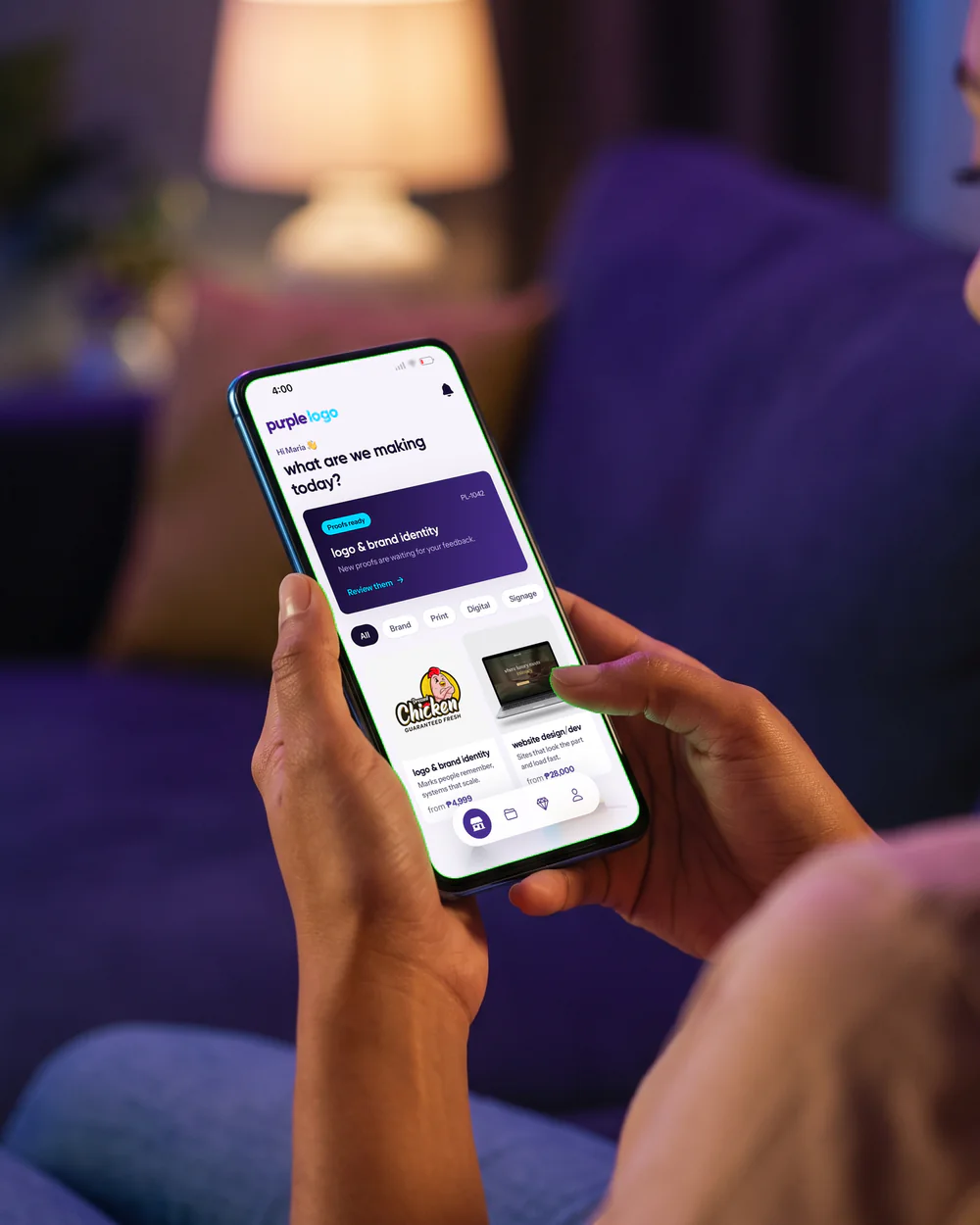 Someone at home on the sofa, holding a phone with the Purple Logo app open on its home screen